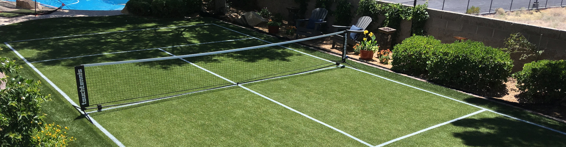 Artificial turf installation used as a backyard tennis court with painted lines and a portable net beside a swimming pool in a desert residential landscape
